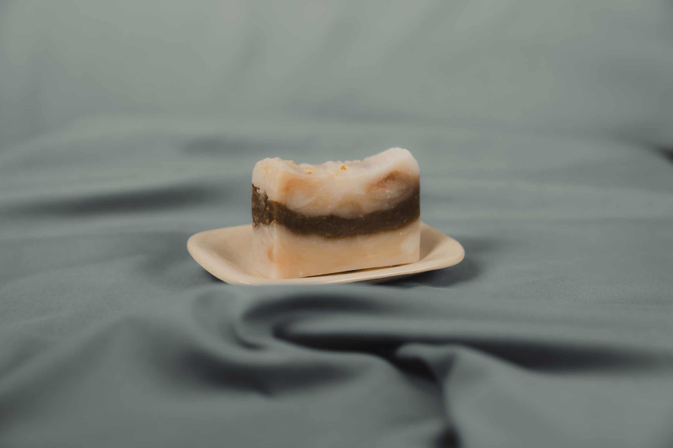 Handmade natural soap bar with brown stripe on a ceramic dish