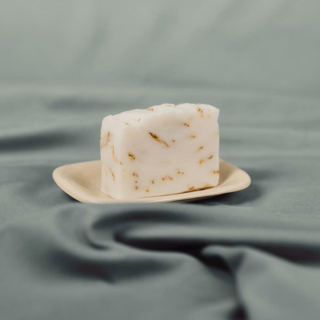 Handmade natural soap bar with calendula petals on a ceramic dish