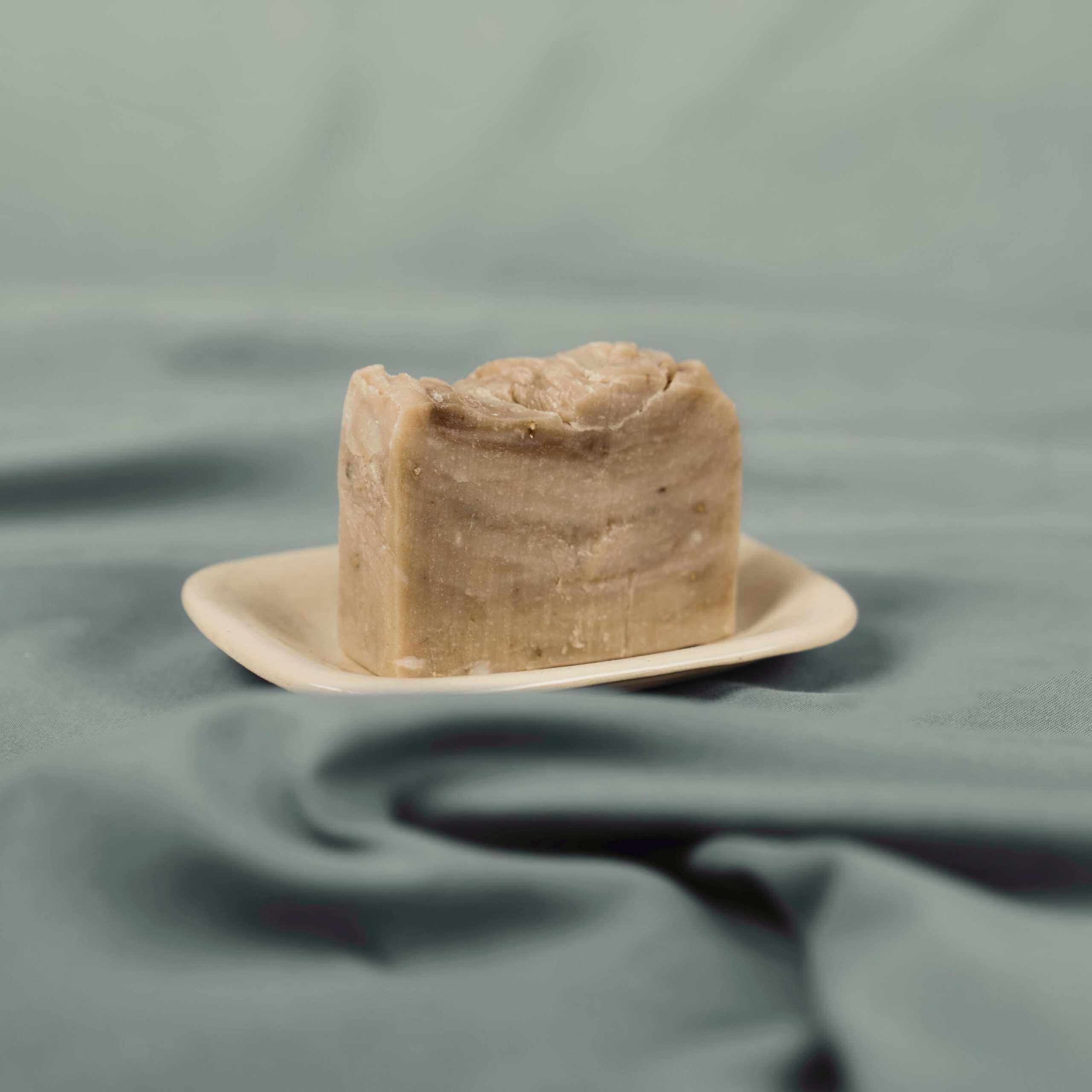 Handmade natural soap bar with brown clay on a ceramic dish
