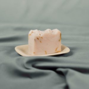 Handmade natural soap bar with soft pink and yellow flecks on a ceramic dish