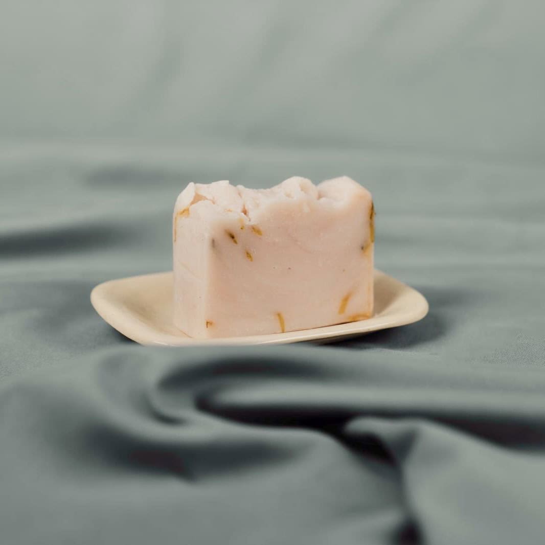 Handmade natural soap bar with soft pink and yellow flecks on a ceramic dish
